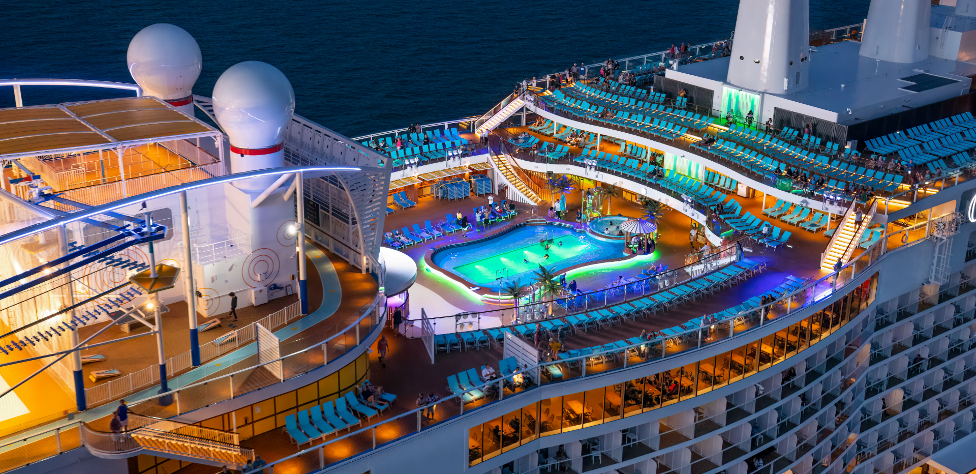 The deck of a Carnival Cruise with a vibrantly lit pool and many chairs.