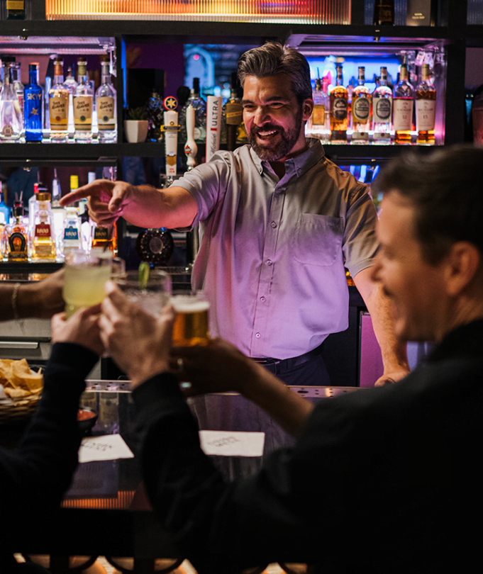 A bartender pointing a laughing with customers.