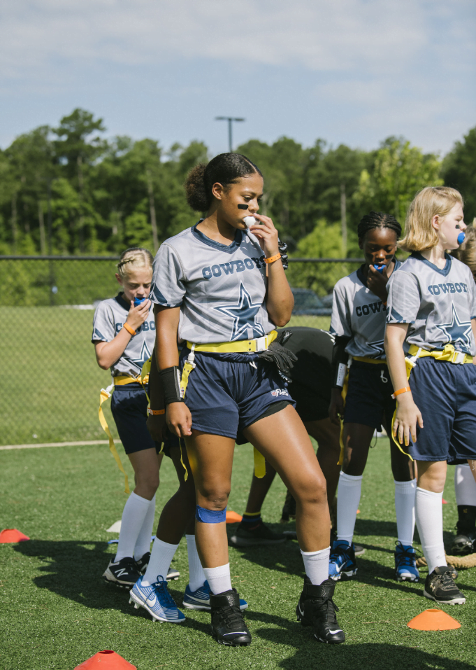 A group of girls wearing Dallas Cowboys shirts on a field.