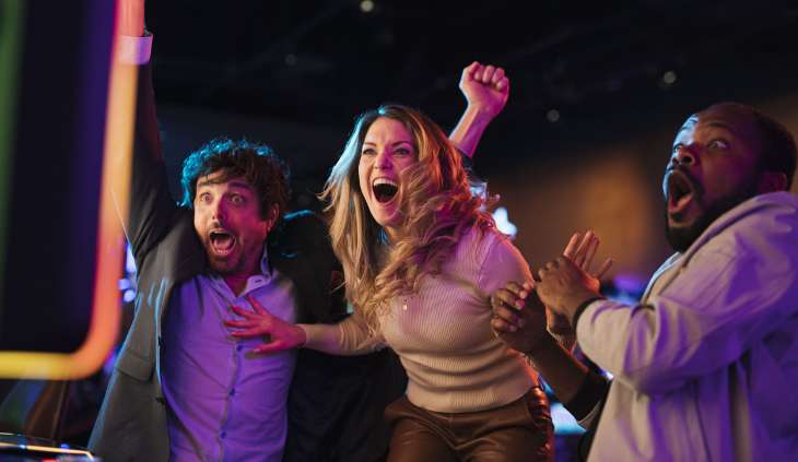 Three people excited in front of an electronic game.